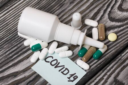 Paper sticker with the inscription COVID-19. Nearby are several pills of various shapes and colors....
