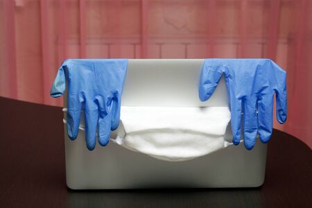 A protective gauze mask is put on the lid of the laptop, rubber gloves hang. A symbol of work in self-isolation during a global epidemic.の写真素材