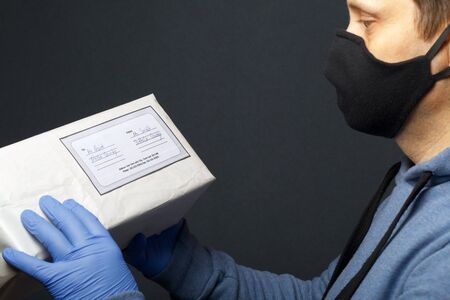 Delivery of correspondence during the period of self-isolation. A man in rubber gloves and a mask holds a delivered parcel in his hands.の写真素材