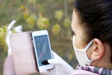 A girl takes pictures on a smartphone in a spring park. On the face is a fabric protective mask....