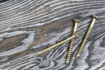 Several yellow metal screws. They lie on pine brushing boards painted black. World Labor Day.