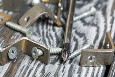 Metal corners with holes for screws. Nearby a screwdriver and screws. They lie on pine brushing...