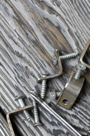 Metal corners with holes for screws. Nearby a screwdriver and screws. They lie on pine brushing...