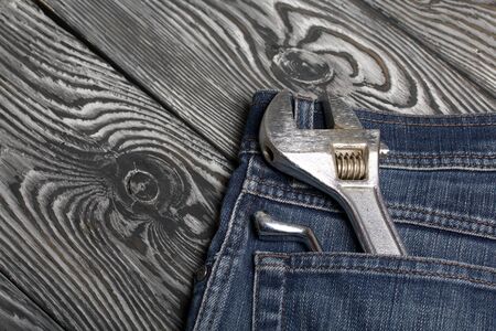 An adjustable wrench and a wrench stick out from the back pocket of the jeans. They lie on black brushed pine boards. Symbol of labor day.の写真素材