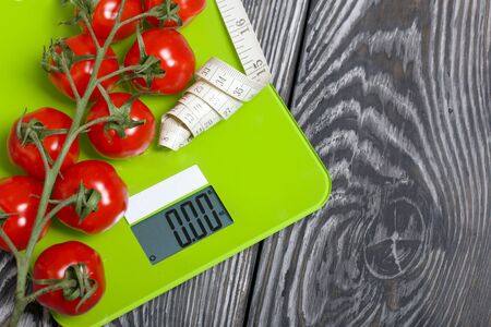Bunches of tomatoes are on the scales. Near the measuring tape. On brushed pine boards. Symbol of World No Diet Day.の写真素材
