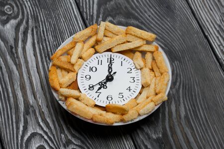 A clock showing seven o'clock in the evening. Lie in a cup with crackers. Against the background of...