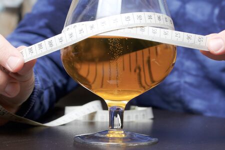 In front of a man is a glass of beer, wrapped in a measuring tape, which he holds in his hands. World No Diet Day.の写真素材