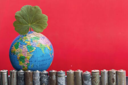 Globe with inscriptions in cyrillic, above it is a green sprout. Around him are spent batteries,...