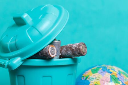 Trash can with lid filled with waste batteries. The batteries are covered with corrosion. Nearby...