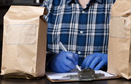 Paper bags with food. Nearby, a man in rubber gloves signs a delivery form. Home delivery during an epidemic.の写真素材