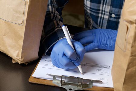 Paper bags with food. Nearby, a man in rubber gloves signs a delivery form. Home delivery during an...