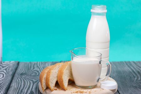 Bottle of milk, a glass of fermented baked milk and slices of ciabatta bread on a cutting board. On brushed pine boards.の写真素材