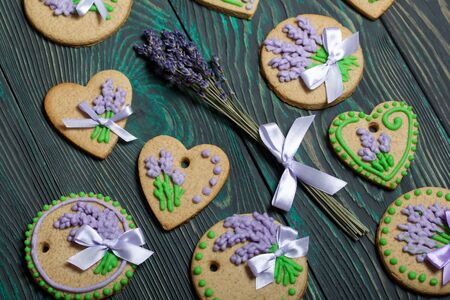 Gingerbread cookies decorated with glaze. On some ribbons tied to a bow. Gingerbread cookies are round and in the shape of a heart. Near a bouquet of lavender. On brushed pine boards.の写真素材