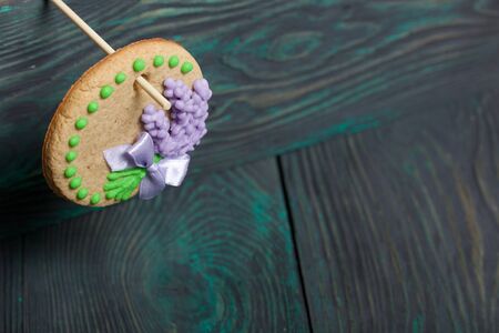 Gingerbread decorated with icing and ribbon tied to a bow. Hanging on a stick. On brushed pine...