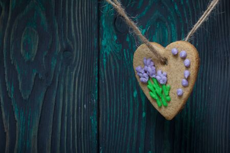 Gingerbread decorated with glaze. Made in the shape of a heart. Hanging on a rope. Against the background of brushed pine boards.の写真素材
