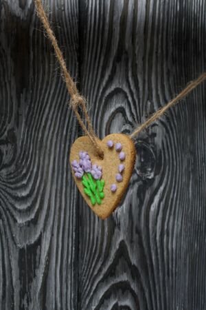 Gingerbread decorated with glaze. Made in the shape of a heart. Hanging on a rope. Against the background of brushed pine boards.の写真素材