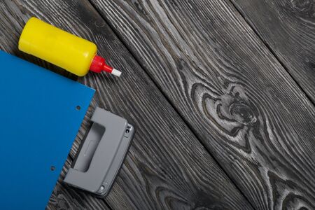 Stationery. Colored paper, hole punch and glue. On brushed pine boards.の写真素材
