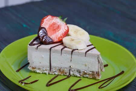 Cheesecake on a plate. Garnished with strawberries, bananas and chocolate. On brushed pine boards...