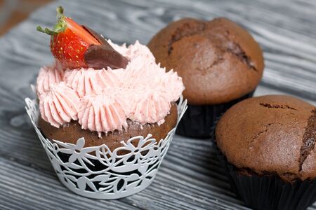 Chocolate cupcakes with strawberry cream. Decorated with half strawberries in chocolate. Next to the...