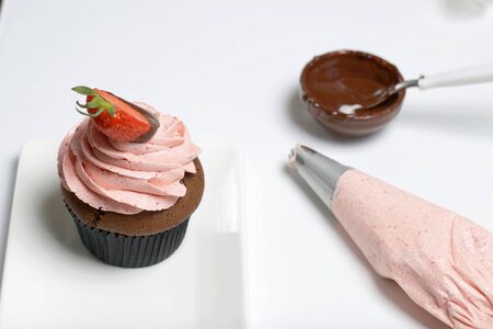 Chocolate cupcakes with strawberry cream. Decorated with half strawberries in chocolate. Next to the blanks and ingredients for cupcakes.の写真素材