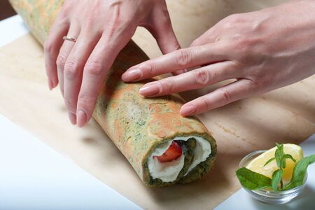A woman wraps strawberries in a spinach and mint cake. Ingredients for cooking.の写真素材