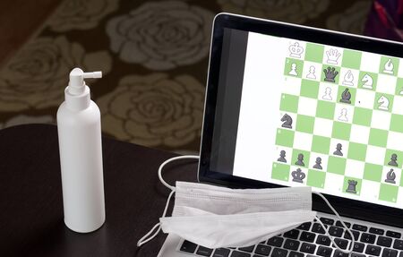 Chess task on laptop screen online. Near antibacterial spray and medical mask. Leisure in...