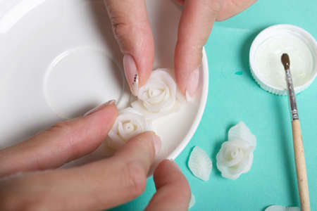 Roses with petals made of white polymer clay. A woman sticks them on a saucer. Crafts from polymer clay.の写真素材