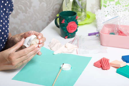 Roses with petals made of white polymer clay. A woman sticks them on a mug. Crafts from polymer clay.の写真素材
