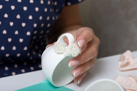 Roses with petals made of white polymer clay. A woman sticks them on a mug. Crafts from polymer clay.の写真素材