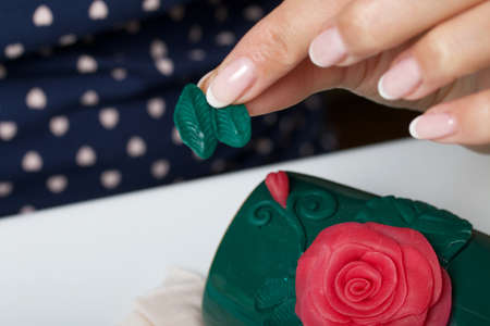Woman glues polymer clay roses to a mug. Polymer clay of different colors. Crafts from polymer clay.