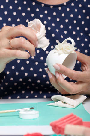 Roses with petals made of white polymer clay. A woman sticks them on a mug. Crafts from polymer...