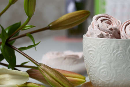 Homemade zephyr of various shapes. In a mug and on the surface of the table. Near a lily with...