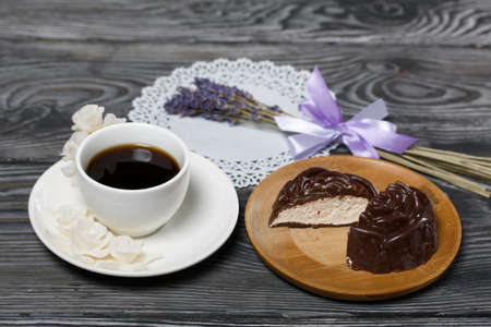 A cup of black coffee on a saucer. Nearby zephyr in chocolate, cut in half, a slice is visible....