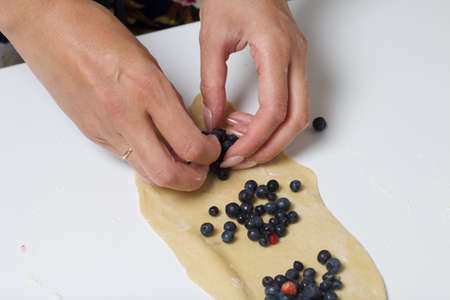 A woman prepares dumplings with blueberries. Puts berries into rolled dough. Close-up shot.