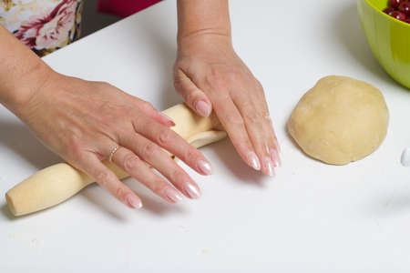 A woman rolls out the dough for making dumplings stuffed with blueberries and cherries. Berries in...
