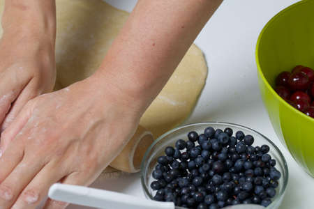 A woman rolls out the dough for making dumplings stuffed with blueberries and cherries. Berries in...
