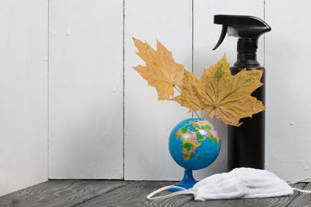 Globe with dried autumn maple leaves. Nearby are protective masks for the duration of a pandemic and a spray bottle with an antiseptic.の写真素材