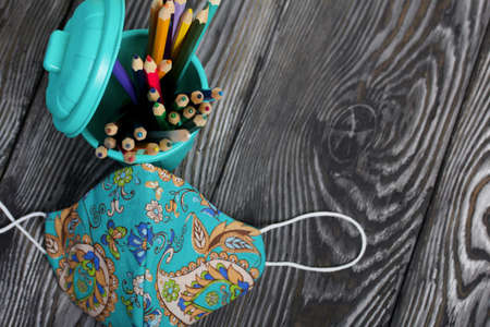 A pencil case in the form of a trash can. It contains colored pencils. Nearby is a protective face mask for the period of a pandemic. Shot from above.の写真素材