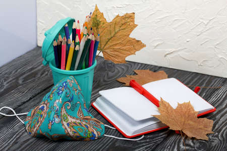 A pencil case in the form of a trash can. It contains colored pencils. Nearby is a notepad and a...