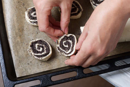 A woman lays curls filled with poppy and walnuts on a baking sheet. Nearby on the table are...
