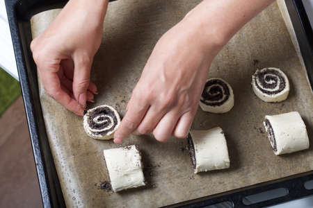 A woman lays curls filled with poppy and walnuts on a baking sheet. Nearby on the table are...