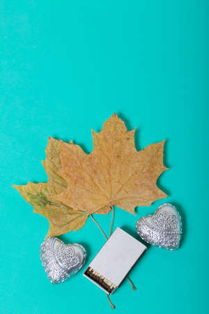 Two decorative candles in the shape of a heart. Next to them are a box of matches and dried maple...