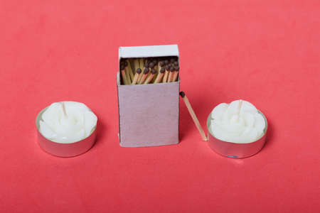 Two decorative candles in the shape of a flower. Next to them is a box of matches. On a coral...