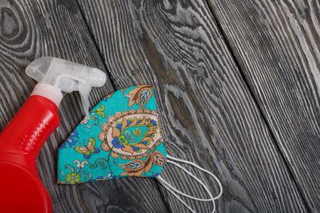 Red plastic bottle with spray. Cleaning spray. Next to the face mask to protect against the virus. On painted pine planks.の写真素材