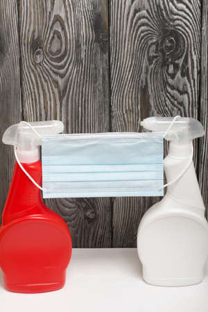 Plastic bottles of white and red color with a spray gun. Cleaning spray. They wear a face mask to...