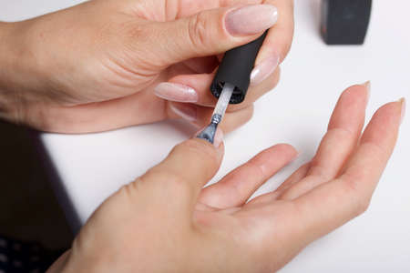 A woman gives herself a manicure. Apply new nail Polish with a brush. Taken in close-up.