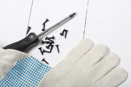 A screwdriver, work gloves, and a handful of screws. On white background.の写真素材