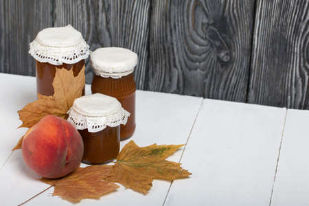Jam in glass jars. Nearby are peaches and dried maple leaves.の写真素材
