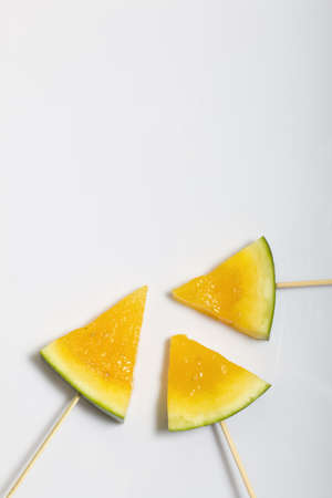 Pieces of yellow watermelon on sticks. Plate on a white surface.の写真素材