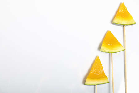 Pieces of yellow watermelon on sticks. Plate on a white surface.